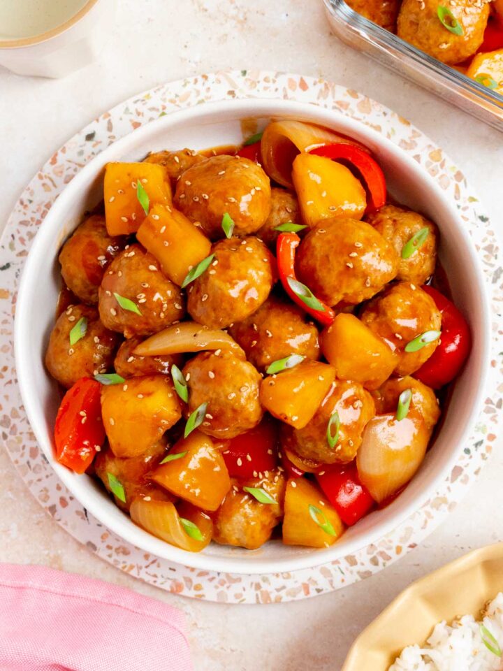 Overhead view of a platter of sweet and sour meatballs topped with green onions and sesame seeds.