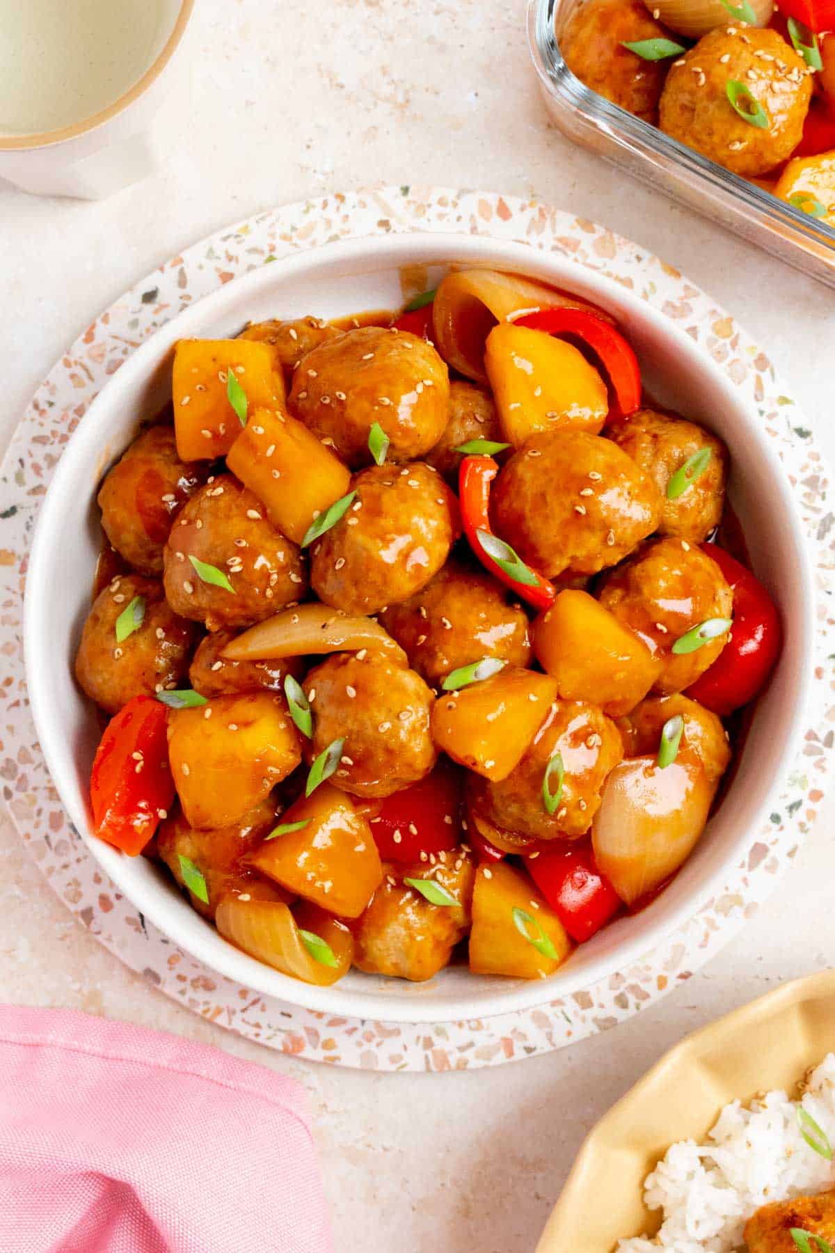 Overhead view of a platter of sweet and sour meatballs topped with green onions and sesame seeds.