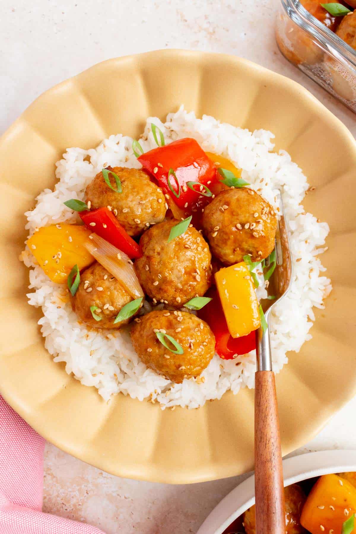 A plate with sweet and sour meatballs on top of rice garnished with sesame seeds and green onions.