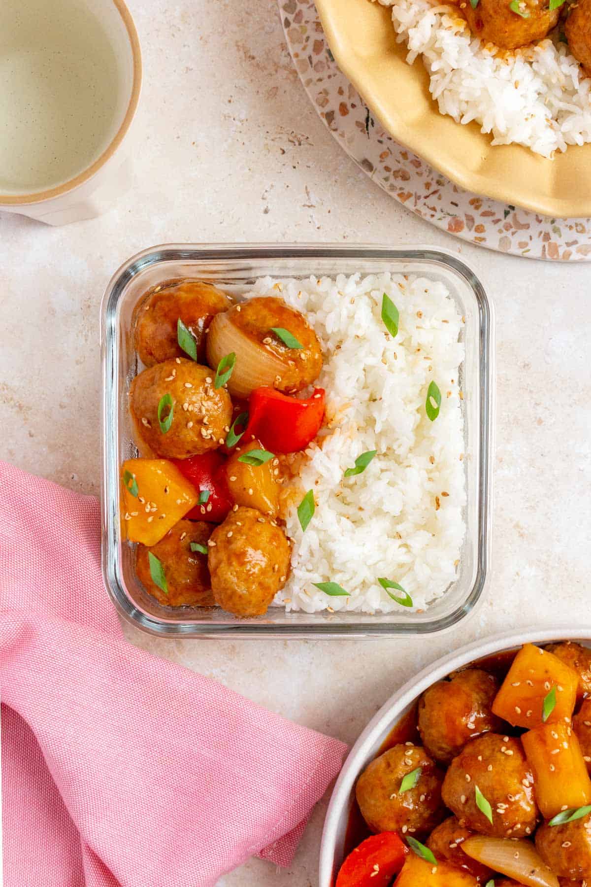 A meal prep container with sweet and sour meatballs along with rice topped with green onions.