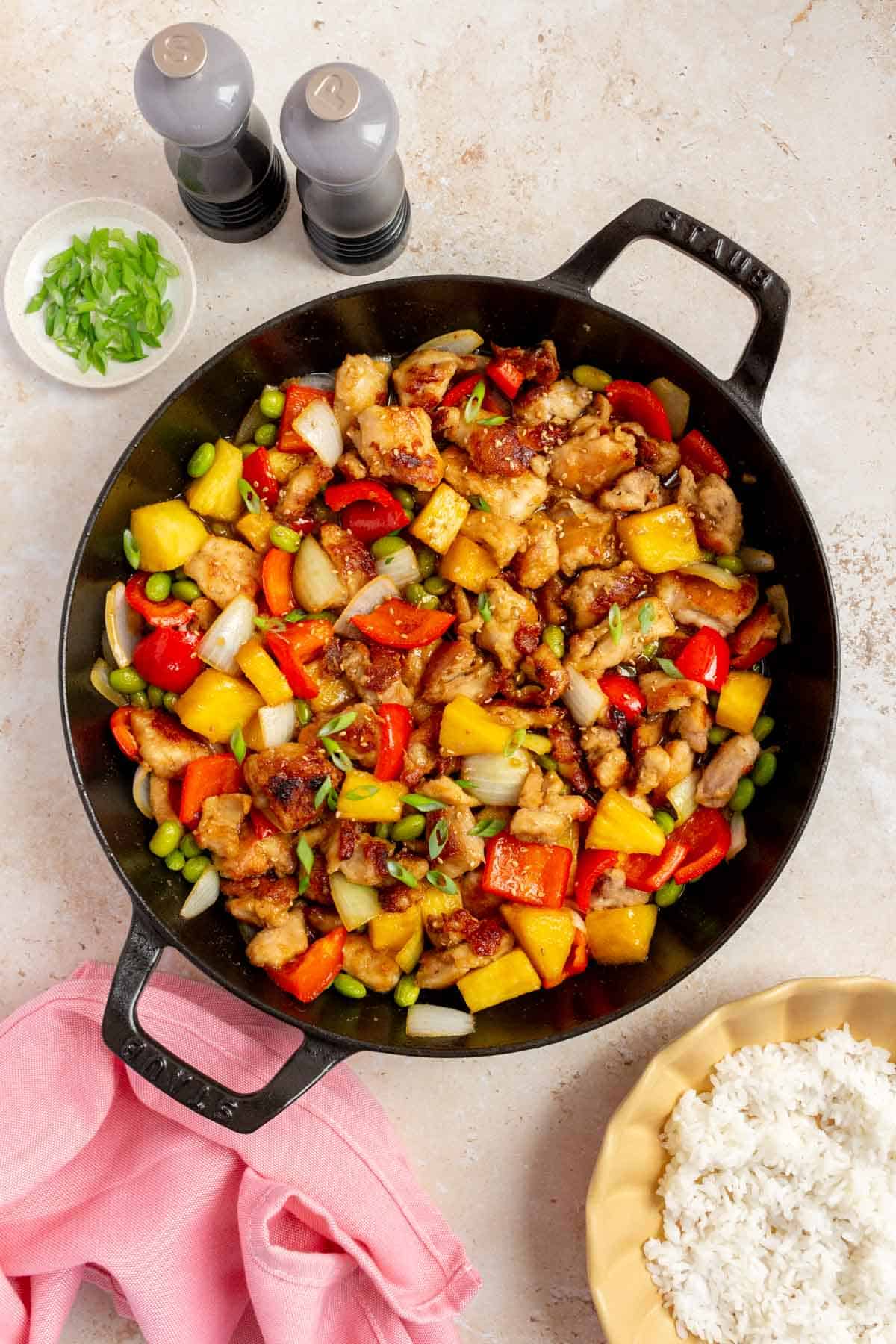 Overhead view of teriyaki pineapple chicken with bell peppers and edamame in a large skillet.
