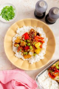 An overhead view of a teriyaki pineapple chicken bowl with rice, garnished with green onions and toasted sesame seeds.
