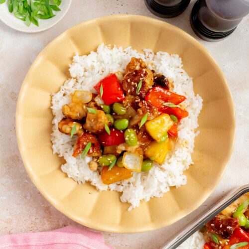 An overhead view of a teriyaki pineapple chicken bowl with rice, garnished with green onions and toasted sesame seeds.