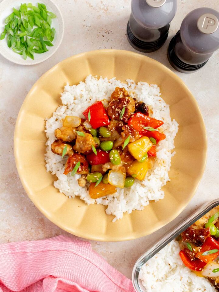 An overhead view of a teriyaki pineapple chicken bowl with rice, garnished with green onions and toasted sesame seeds.