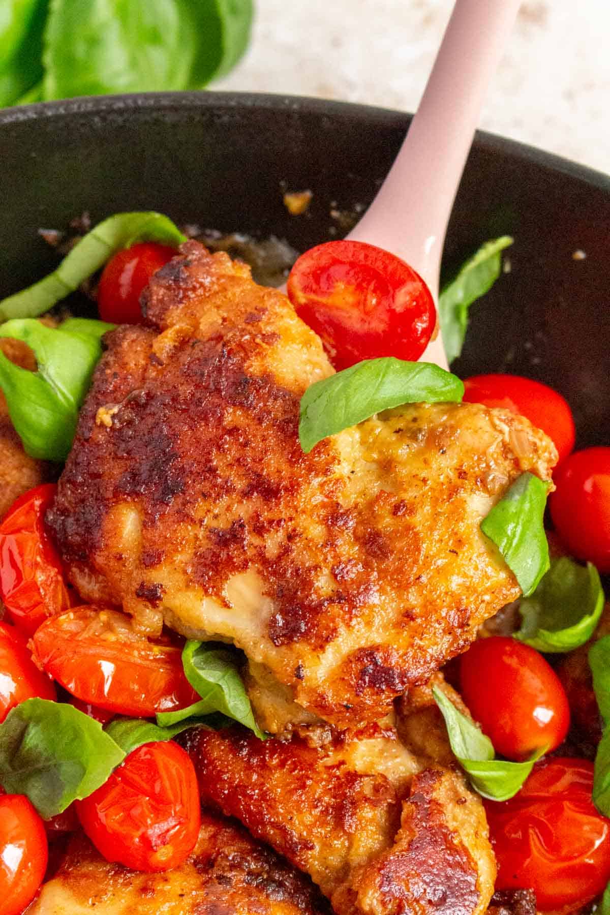 A piece of tomato basil chicken thigh lifted from the skillet.