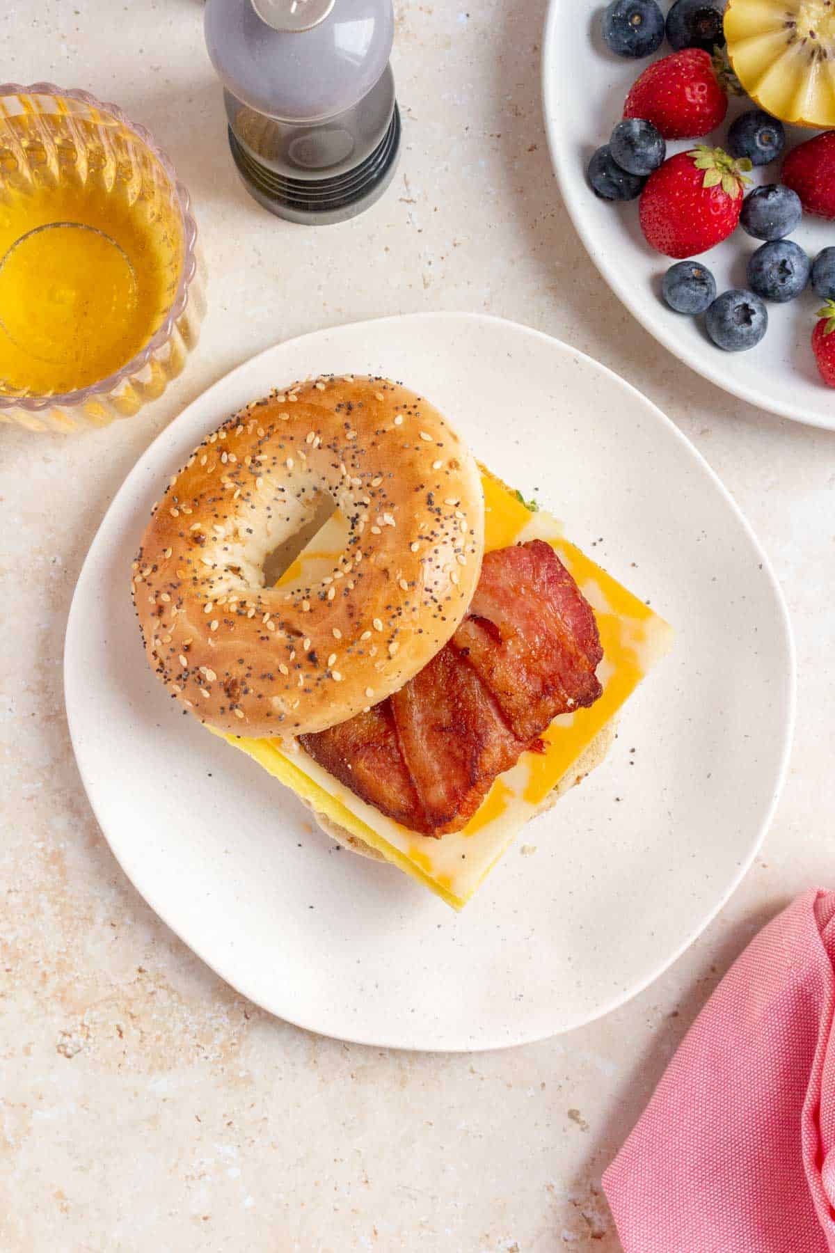 An overhead view of a plate with a bacon, egg, and cheese bagel with the top half of the bagel leaning on the sandwich.