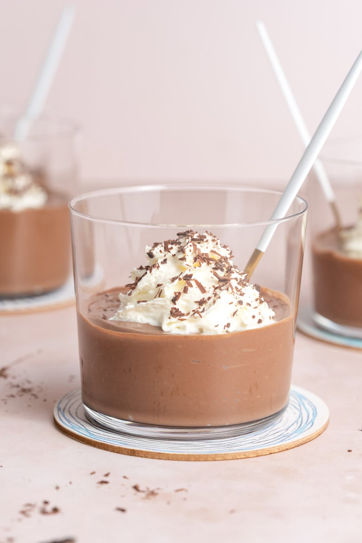 A jar of chocolate tofu pudding on a coaster, topped with whipped cream and shaved chocolate.