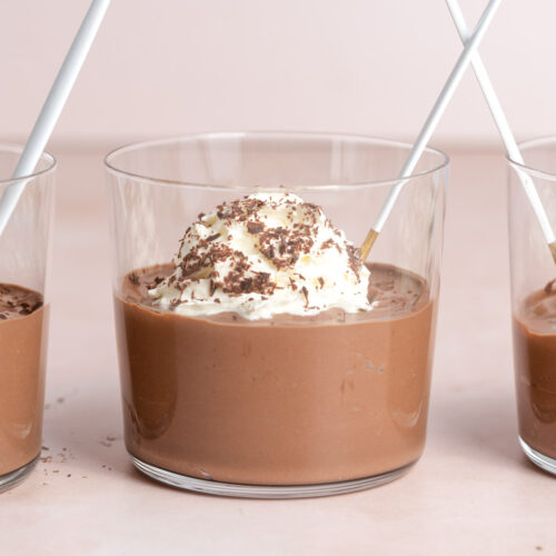 A glass of chocolate tofu pudding topped with whipped cream and shaved chocolate with a spoon inside.