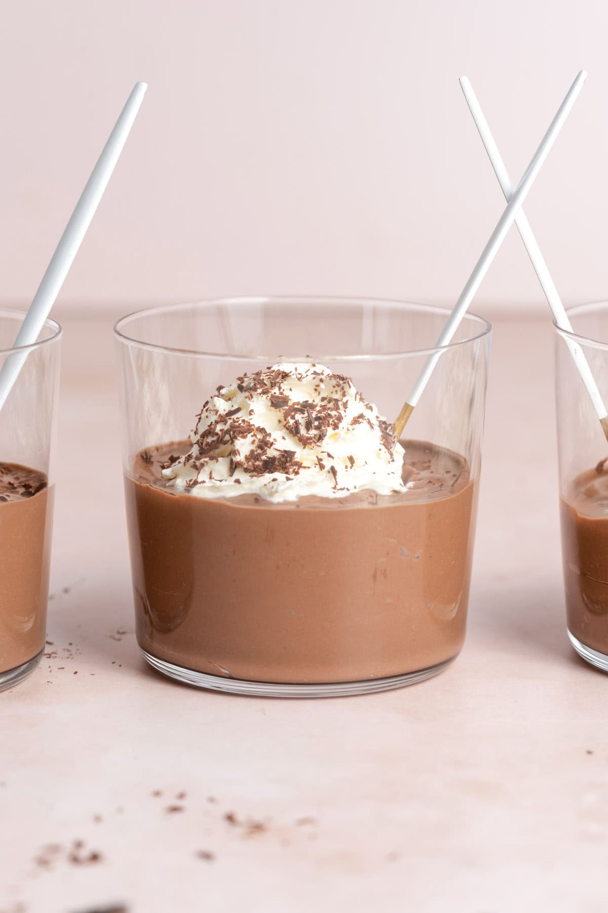 A glass of chocolate tofu pudding topped with whipped cream and shaved chocolate with a spoon inside.