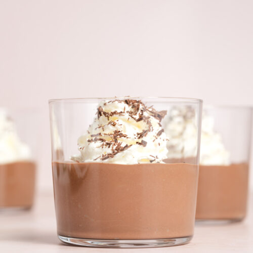 A profile view of a jar of chocolate tofu pudding topped with whipped cream.