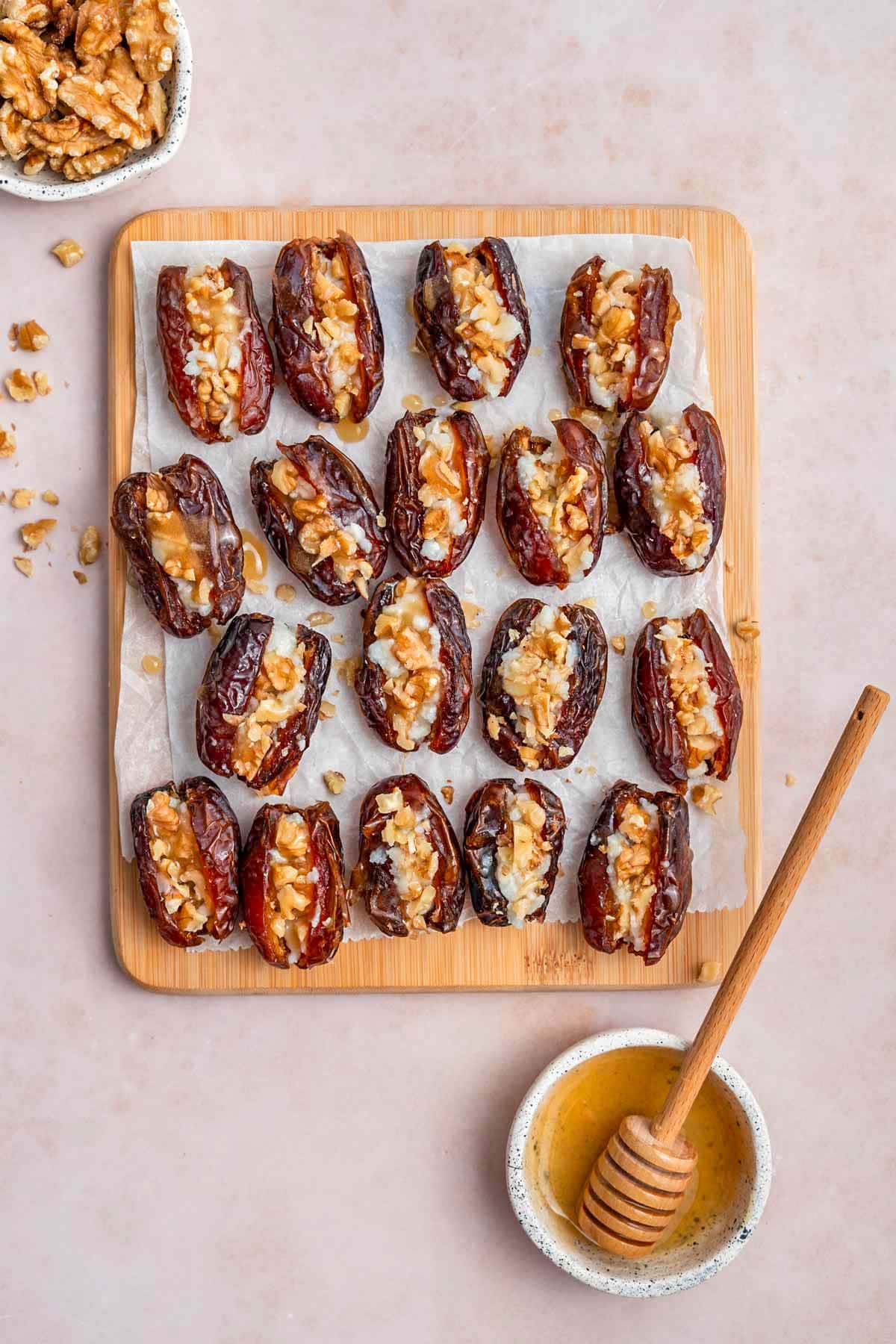 Overhead view of a parchment lined board with goat cheese stuffed dates. A bowl of honey on the side.