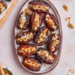 Overhead view of an oval platter containing goat cheese stuffed dates with honey and walnuts on the side.