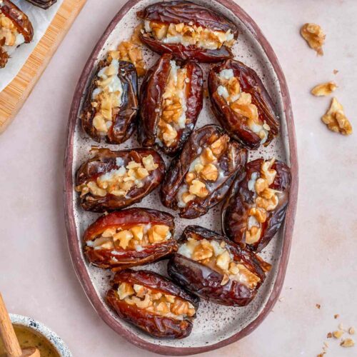 Overhead view of an oval platter containing goat cheese stuffed dates with honey and walnuts on the side.