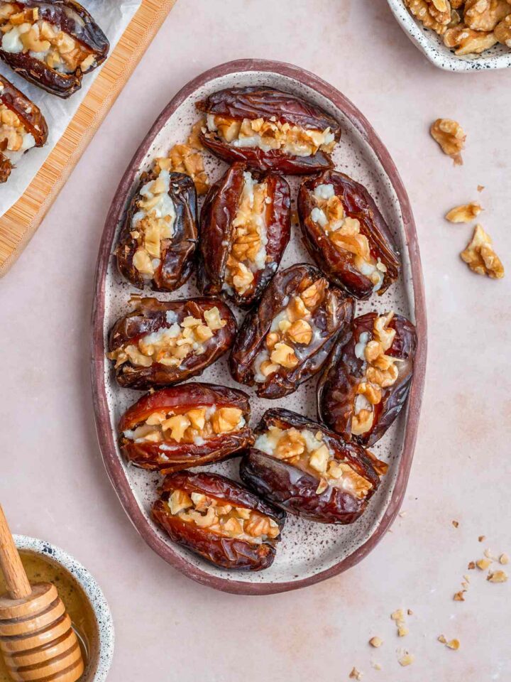 Overhead view of an oval platter containing goat cheese stuffed dates with honey and walnuts on the side.