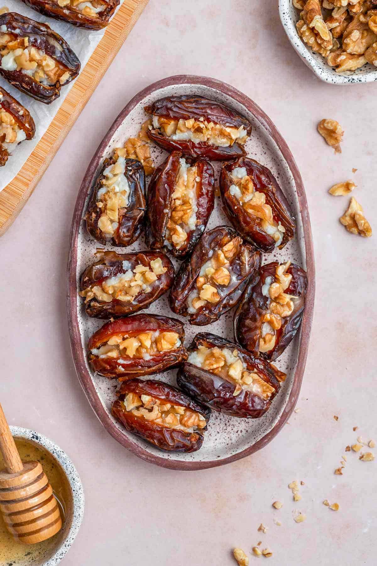 Overhead view of an oval platter containing goat cheese stuffed dates with honey and walnuts on the side.