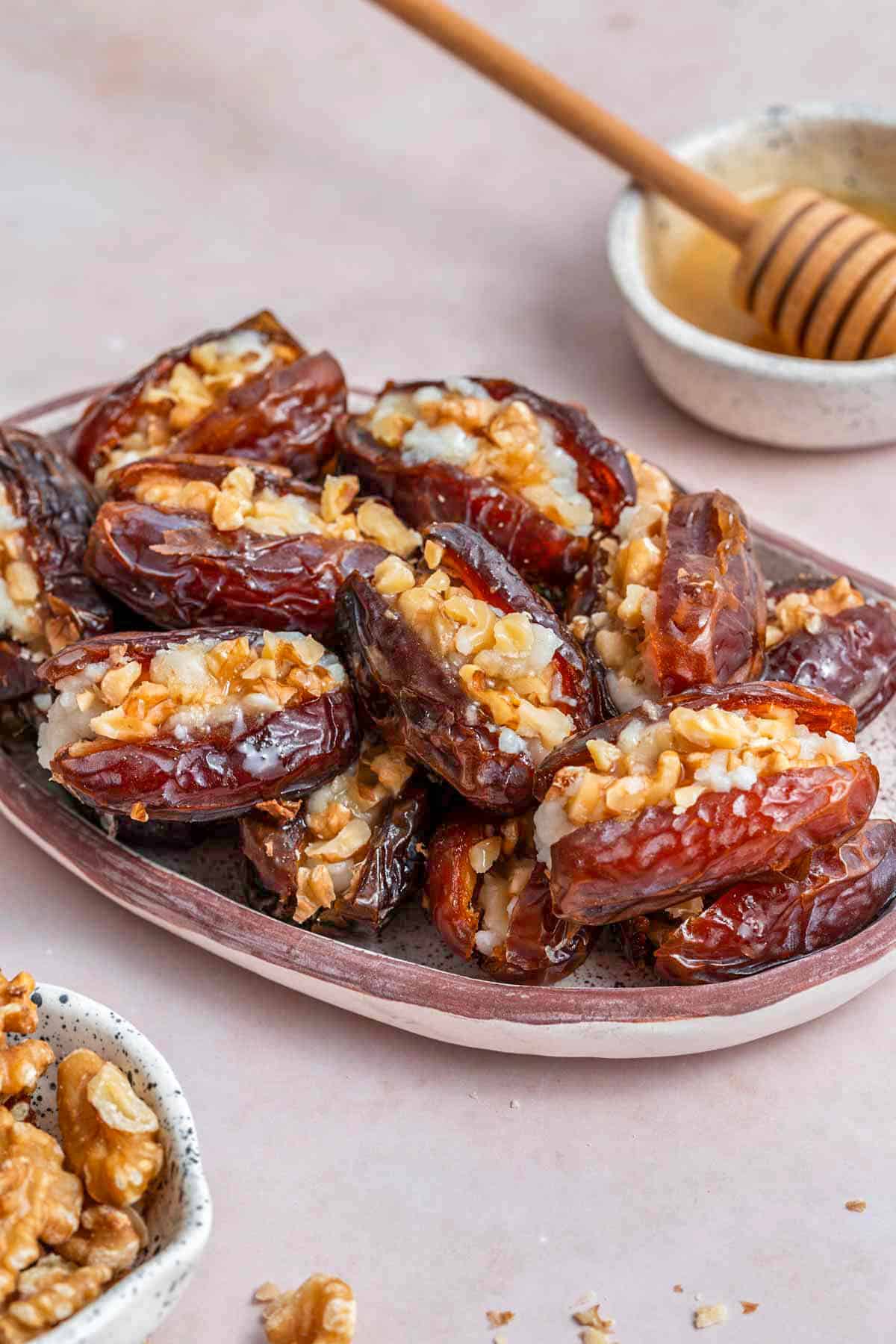 A platter of goat cheese stuffed dates with some walnuts and honey on the side.