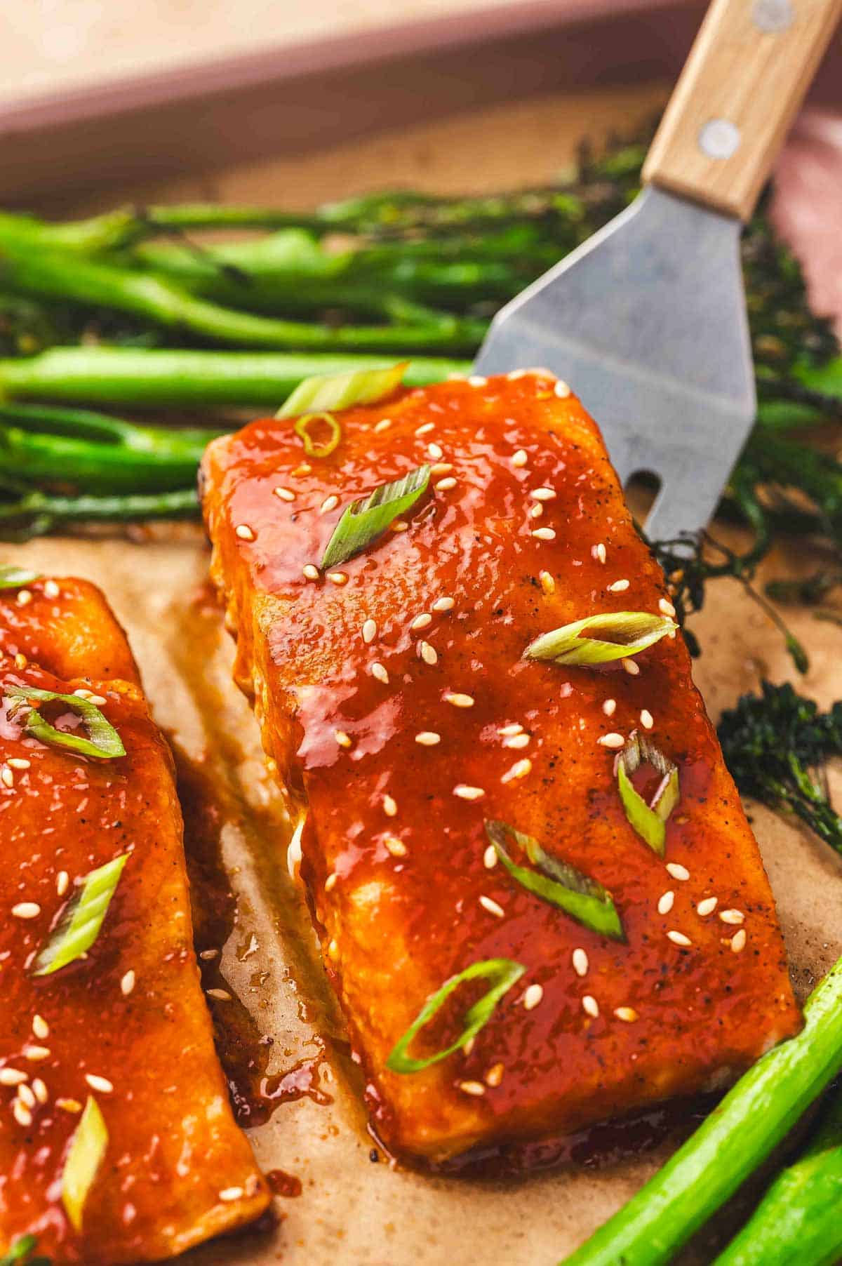 A close up view of gochujang salmon with broccolini with the salmon being lifted.