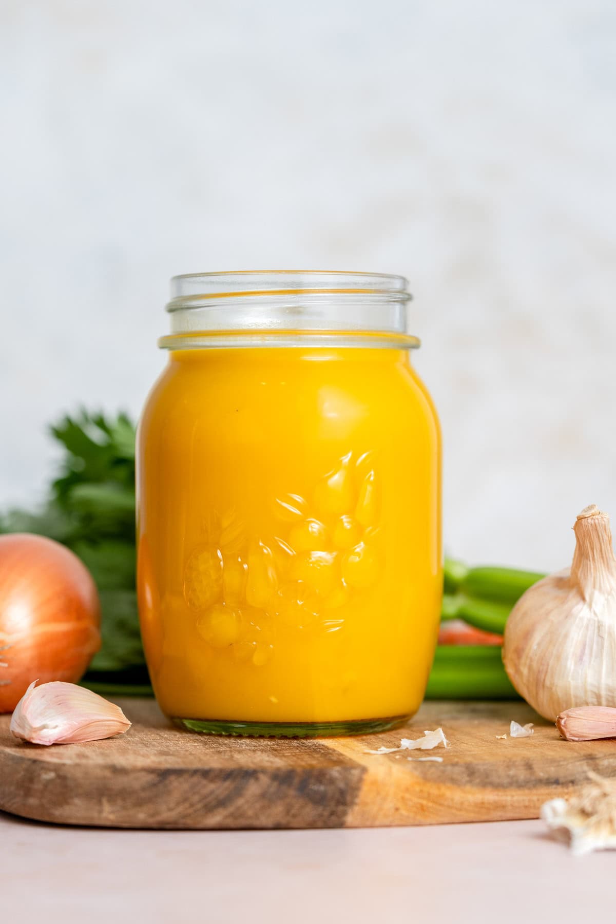 A mason jar of veggie packed broth on a wooden board surrounded by veggies.