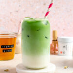 A glass of jasmine matcha with a straw, showing the layer of milk and matcha separated.