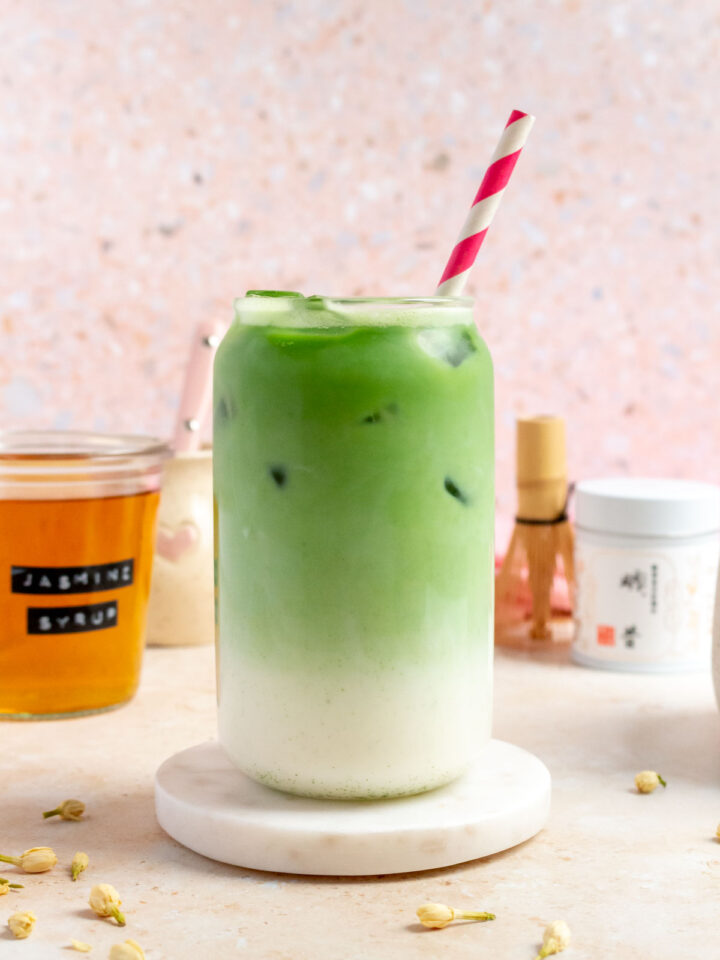 A glass of jasmine matcha with a straw, showing the layer of milk and matcha separated.
