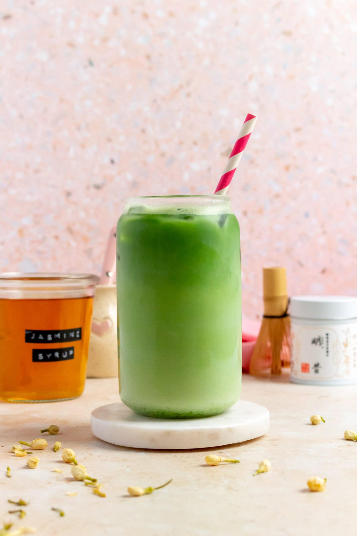 A glass of jasmine matcha latte with a straw on a coaster.