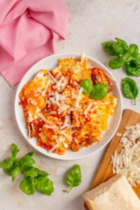 A plate of ravioli lasagna topped with shredded parmesan and basil.