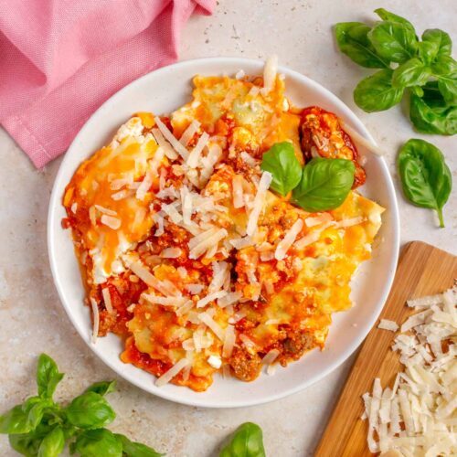 A plate of ravioli lasagna topped with shredded parmesan and basil.