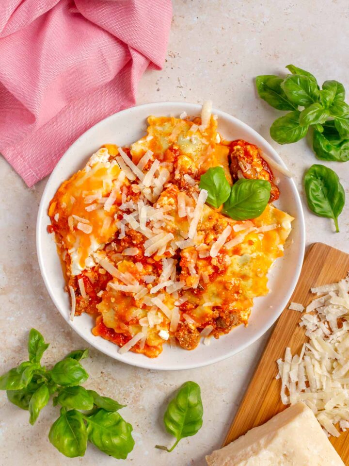 A plate of ravioli lasagna topped with shredded parmesan and basil.