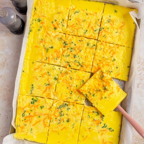 Overhead view of sheet pan cottage cheese eggs sliced in the sheet pan with one slice lifted up.