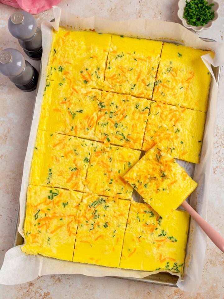 Overhead view of sheet pan cottage cheese eggs sliced in the sheet pan with one slice lifted up.