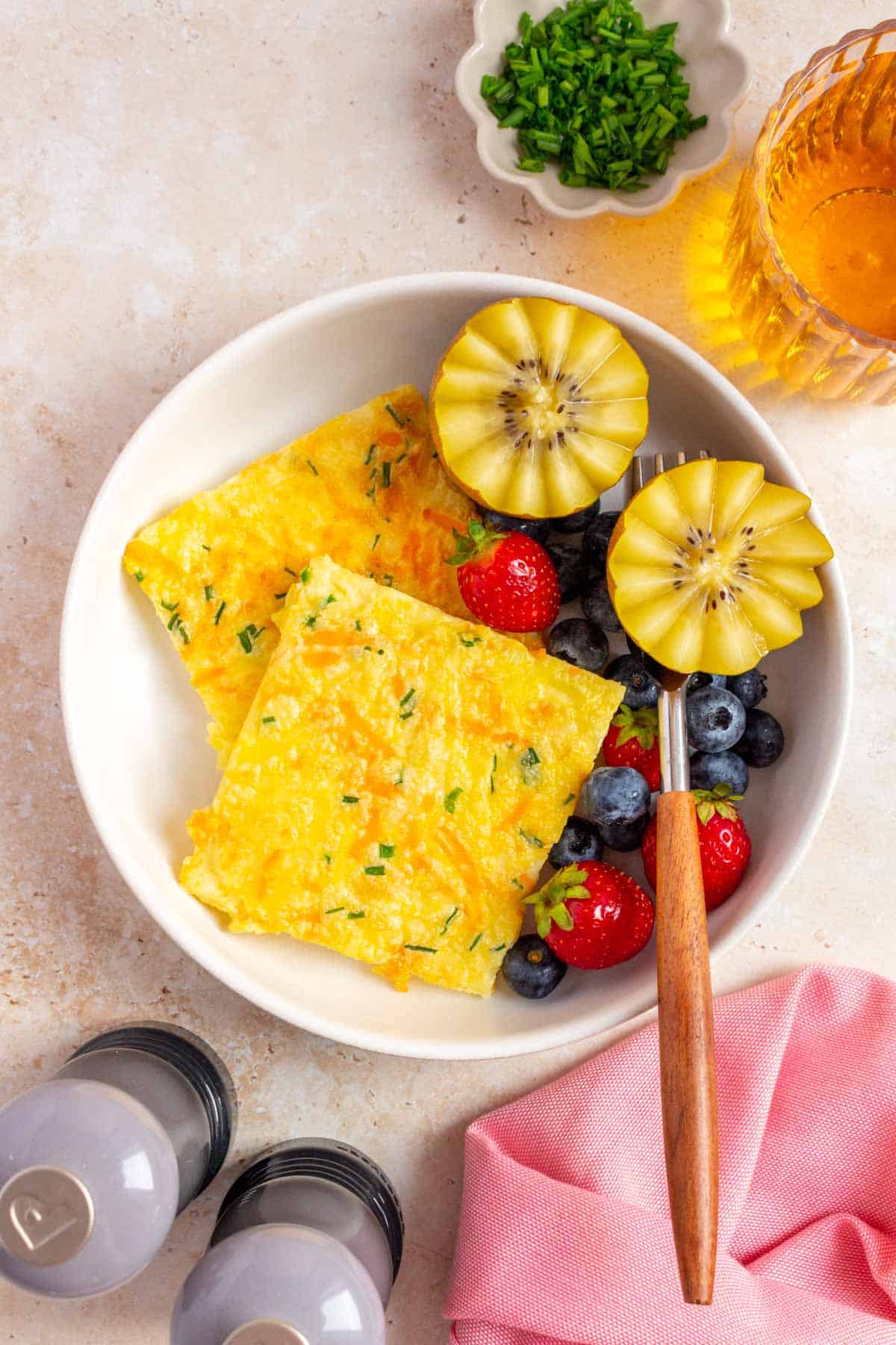A plate with two slices of sheet pan cottage cheese eggs with berries, kiwi, and a fork.