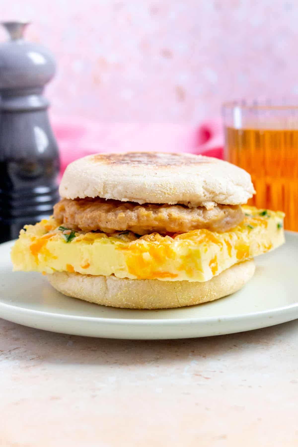 A side view of a breakfast sandwich with a slice of sheet pan cottage cheese eggs and sausage between an english muffin.