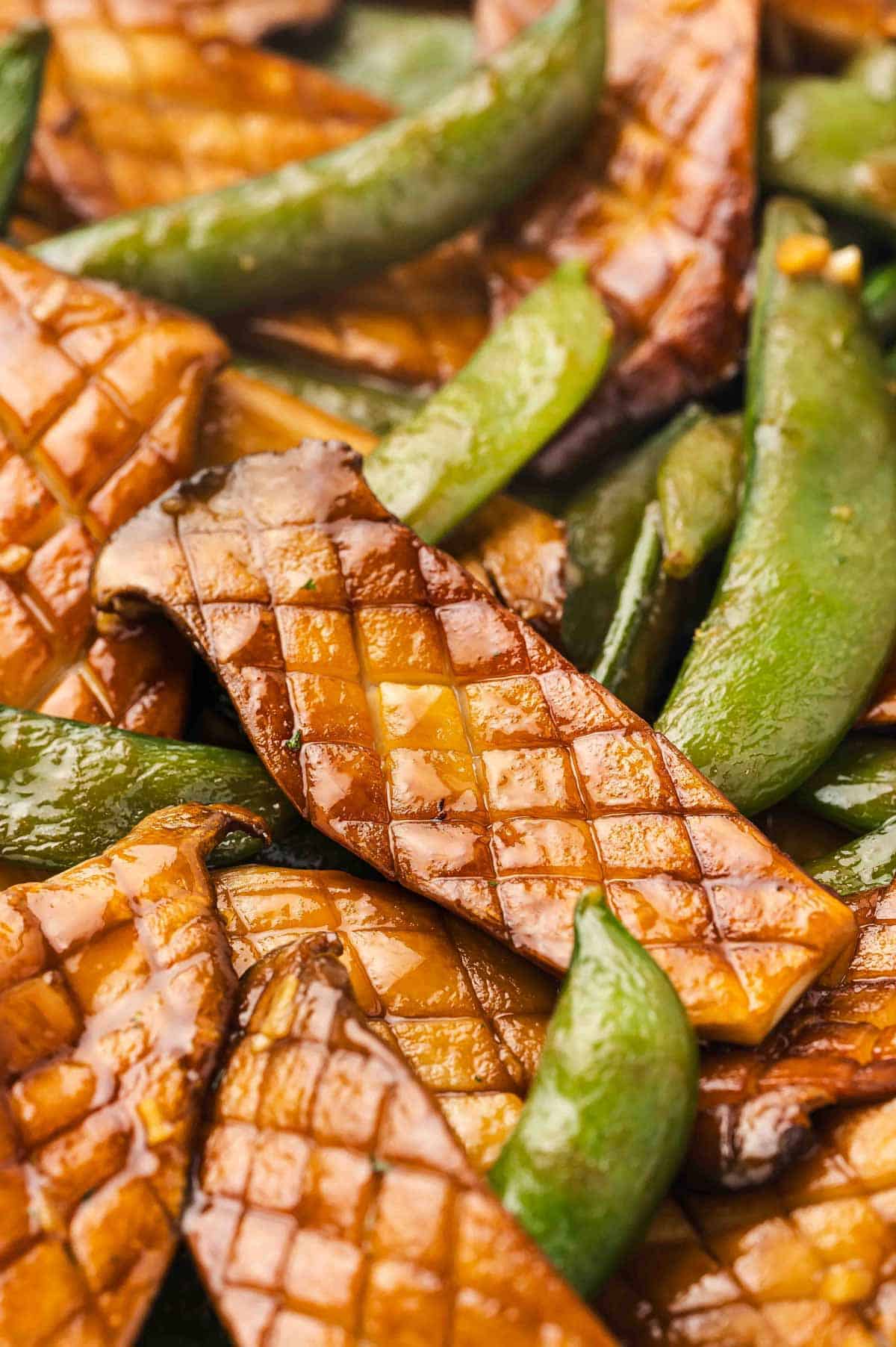 A close up view of baby king oyster mushroom and snap peas stir fry, highlighting the cross hatch marks on the mushrooms.