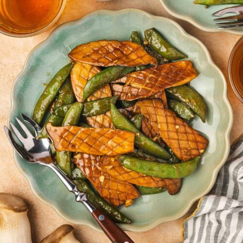 Overhead view of a plate of baby king oyster mushroom and snap peas stir fry with a fork.