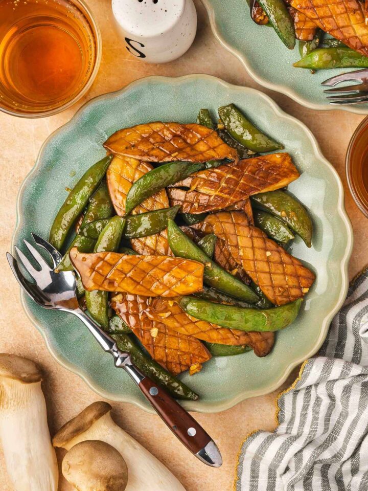 Overhead view of a plate of baby king oyster mushroom and snap peas stir fry with a fork.
