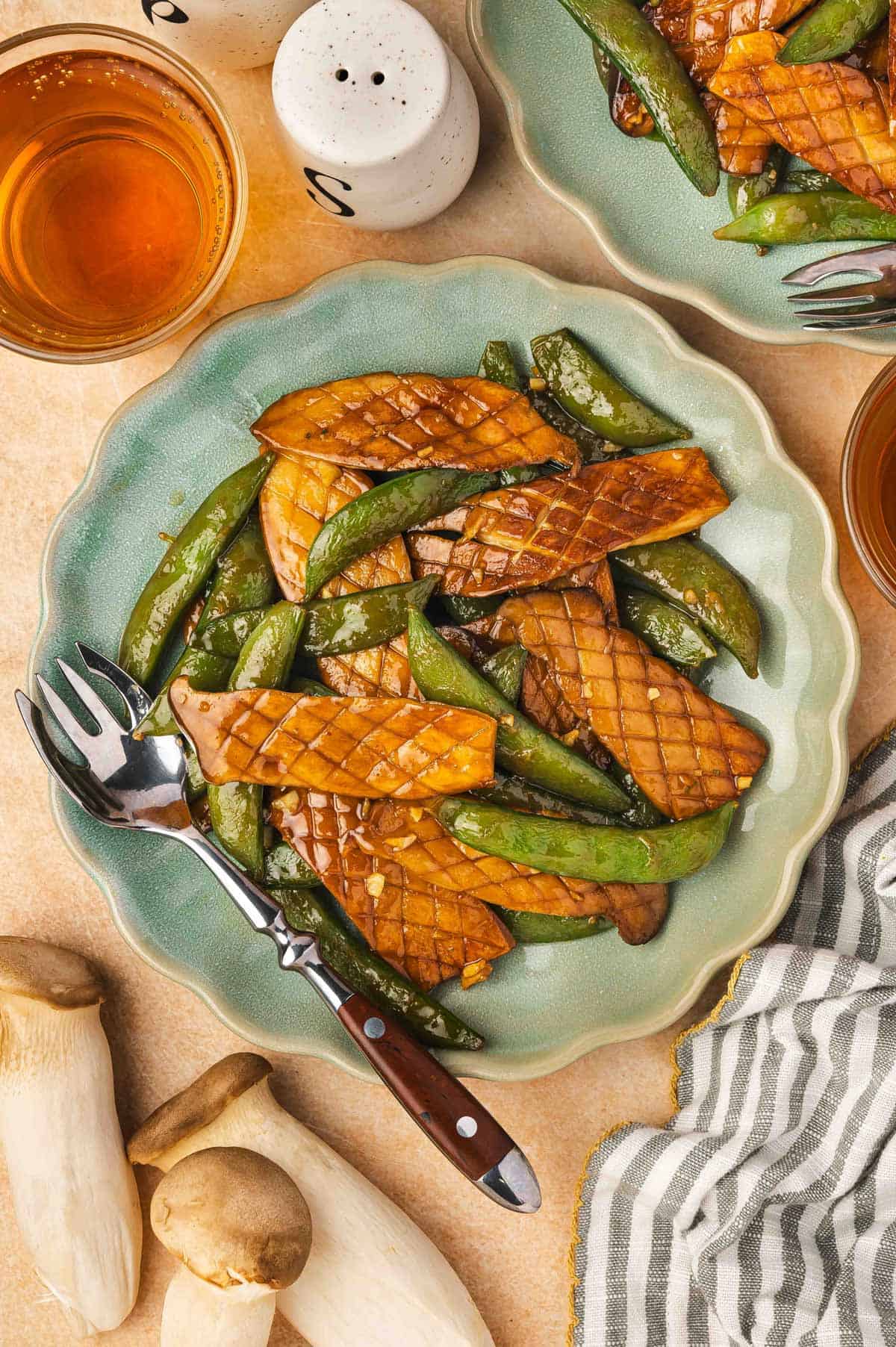 Overhead view of a plate of baby king oyster mushroom and snap peas stir fry with a fork.