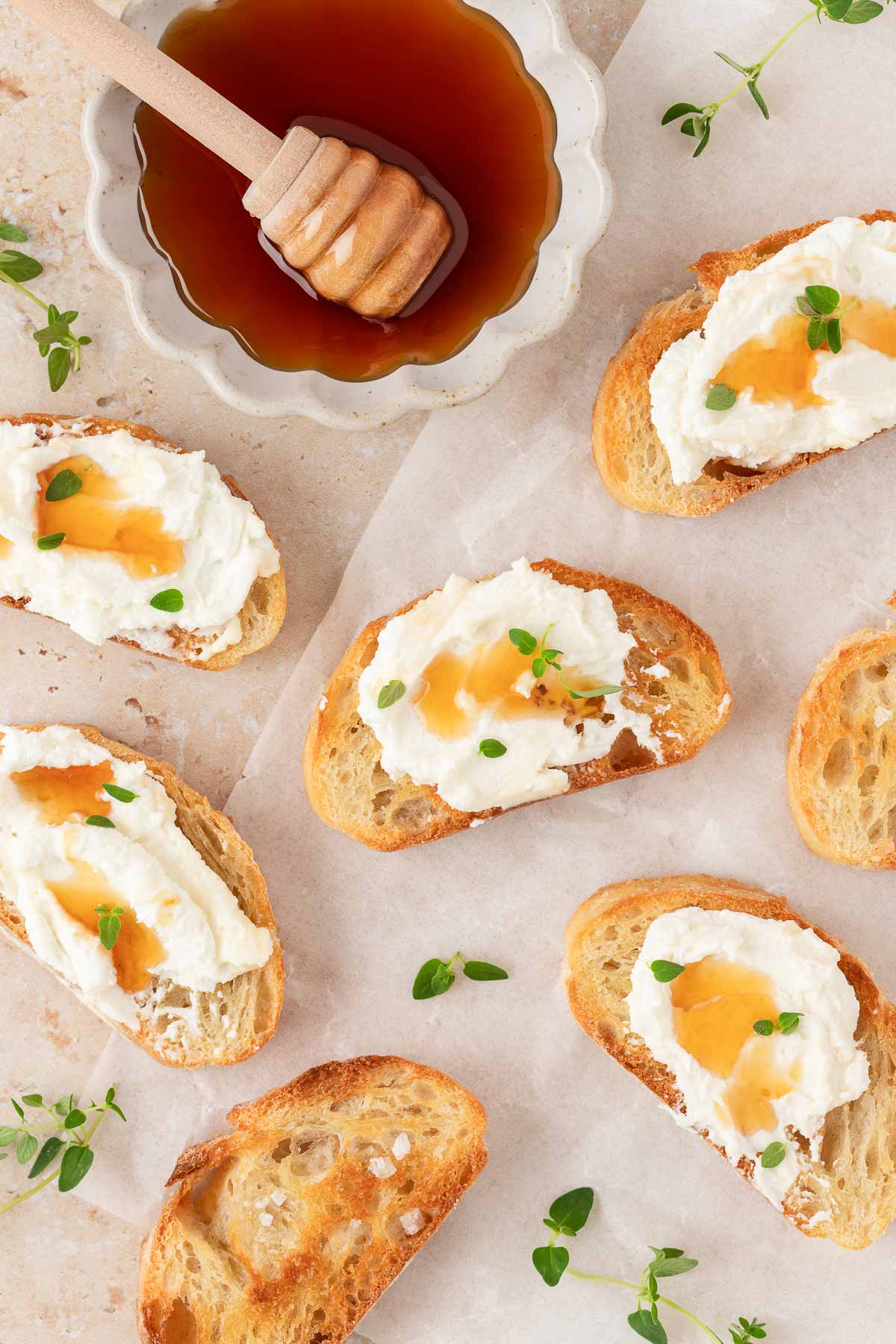 Multiple crostini with whipped goat cheese topped with hot honey and fresh thyme. A bowl of honey off to the side.