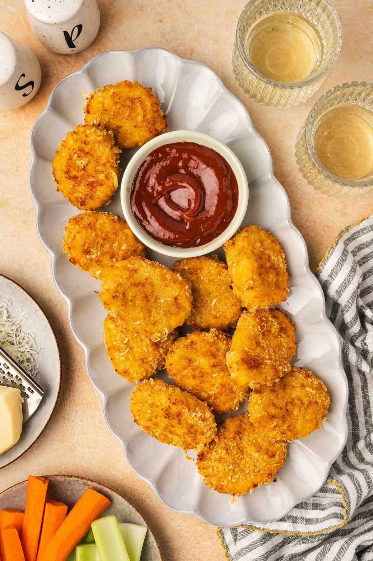 A scalloped platter with cheesy chicken nuggets and a bowl of ketchup.
