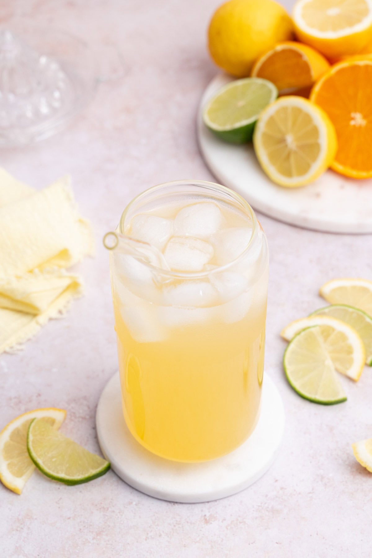 A glass of homemade lemon lime electrolyte drink with ice. Cut citrus in the background.