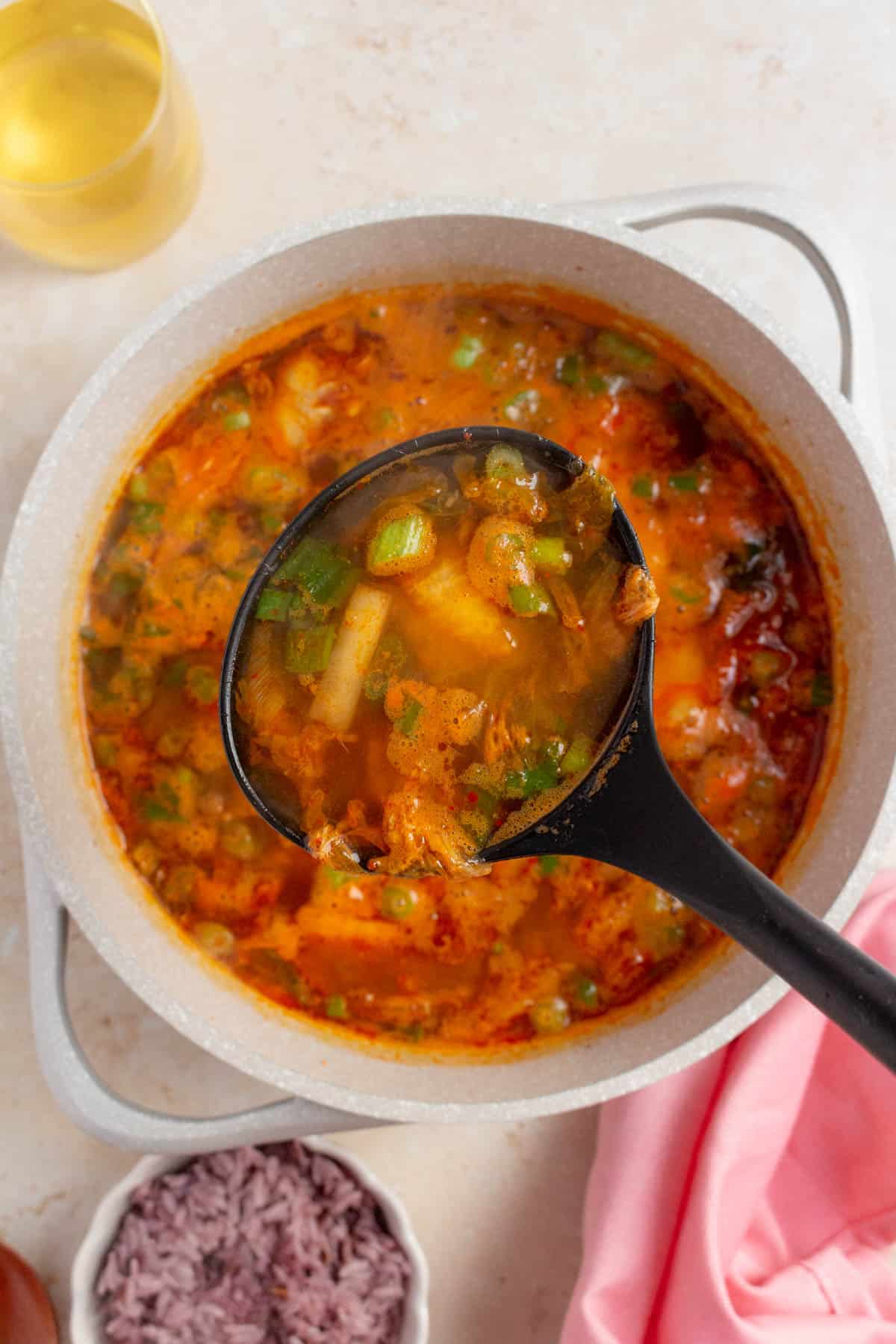 A ladle lifting up a scoop of tuna kimchi stew from a pot.