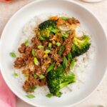 Overhead view of a plate of rice topped with gochujang beef and broccoli and kimchi with green onion garnish.