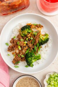 Overhead view of a plate of rice topped with gochujang beef and broccoli and kimchi with green onion garnish.