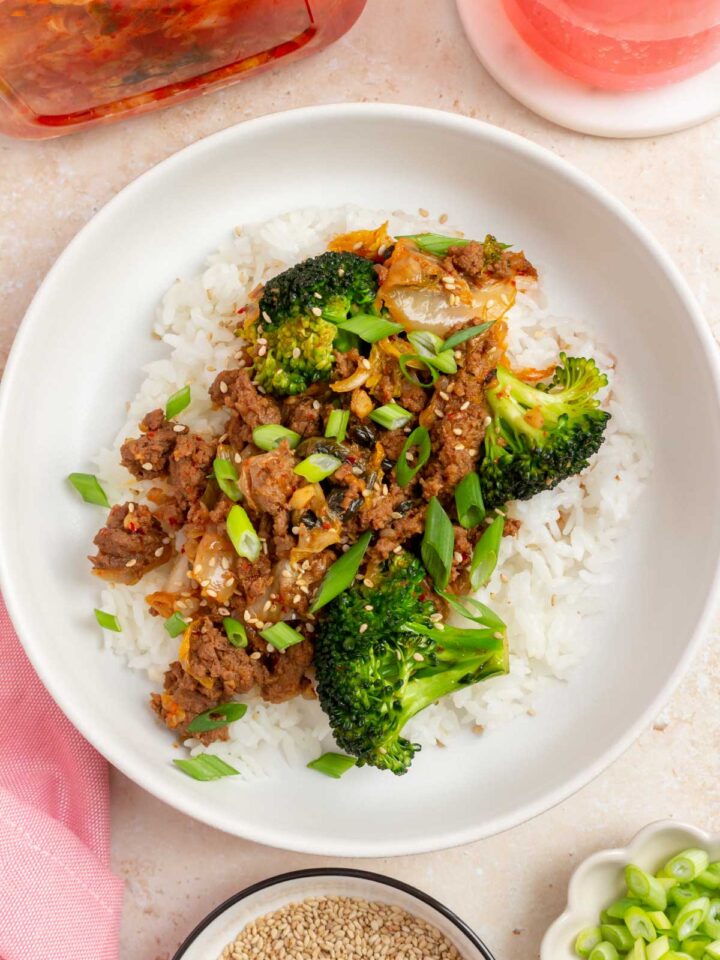 Overhead view of a plate of rice topped with gochujang beef and broccoli and kimchi with green onion garnish.