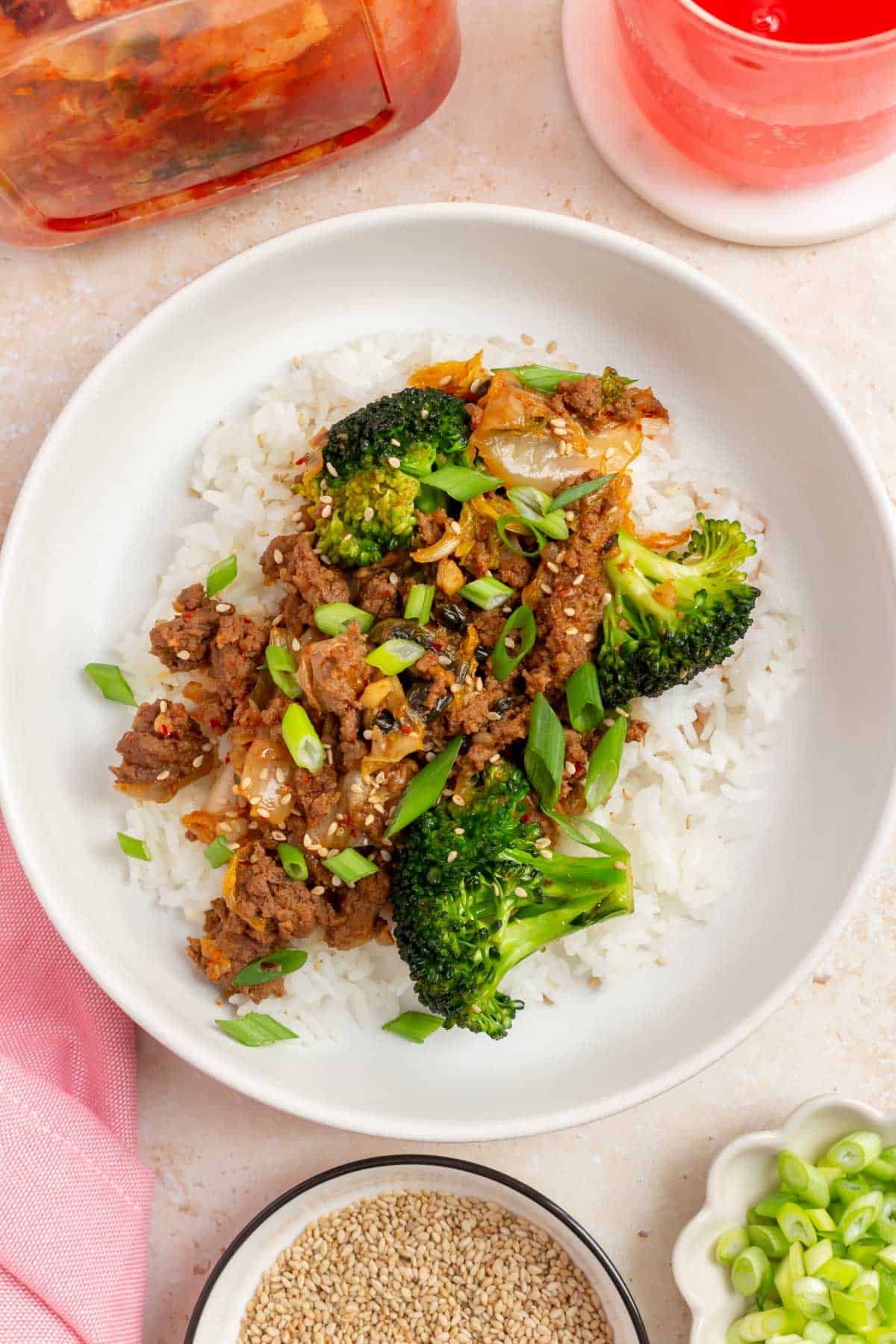 Overhead view of a plate of rice topped with gochujang beef and broccoli and kimchi with green onion garnish.