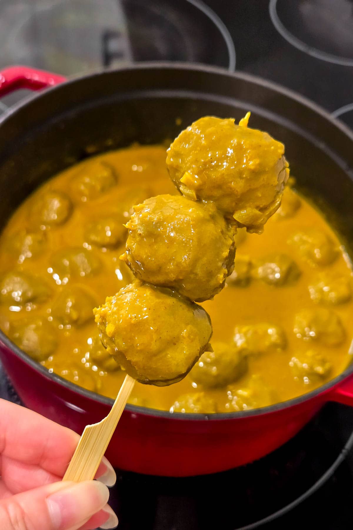 Three beef balls on a skewer coated in a hong kong curry sauce. 