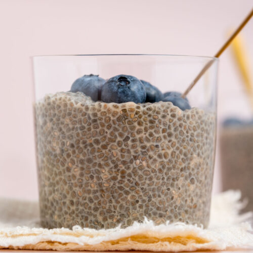A close up profile view of a jar of jasmine chia pudding topped with fresh blueberries.
