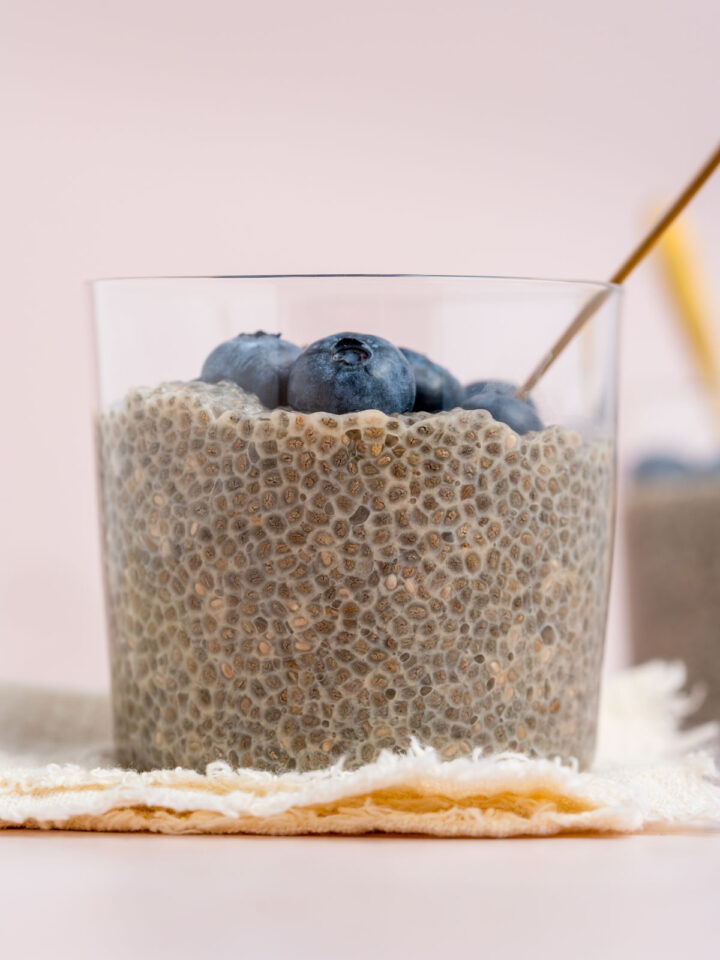 A close up profile view of a jar of jasmine chia pudding topped with fresh blueberries.