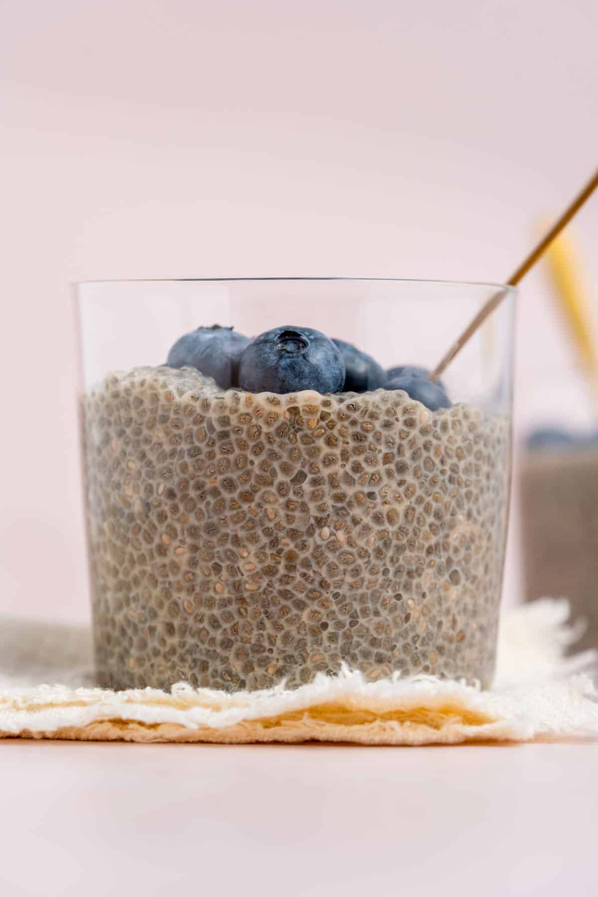 A close up profile view of a jar of jasmine chia pudding topped with fresh blueberries.