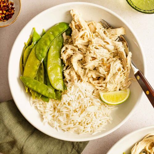 Overhead view of a bowl of rice and snow peas with shredded instant pot thai green curry chicken and a lime.