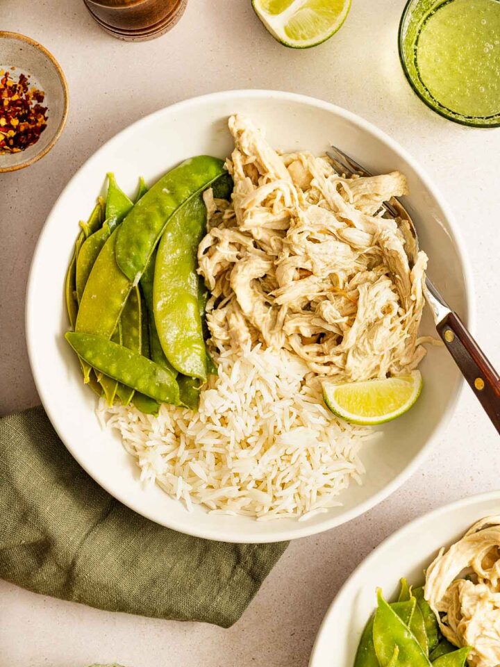 Overhead view of a bowl of rice and snow peas with shredded instant pot thai green curry chicken and a lime.